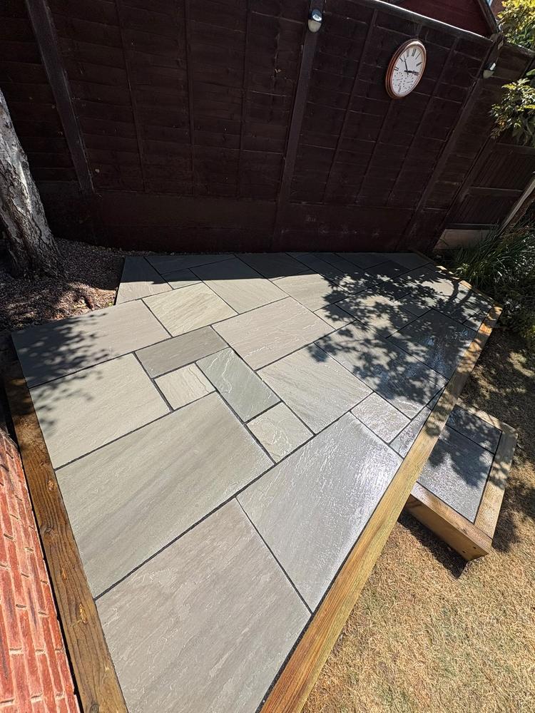After: the same corner finished as a raised sandstone patio with timber edging