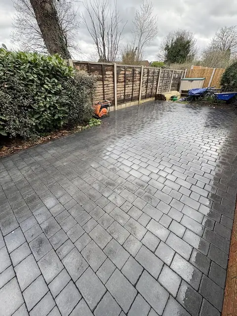 A large block paved area laid between a hedge and a new fence