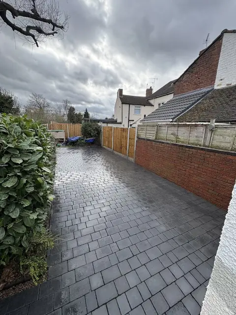 A block paved path running down the side of a house beside a hedge