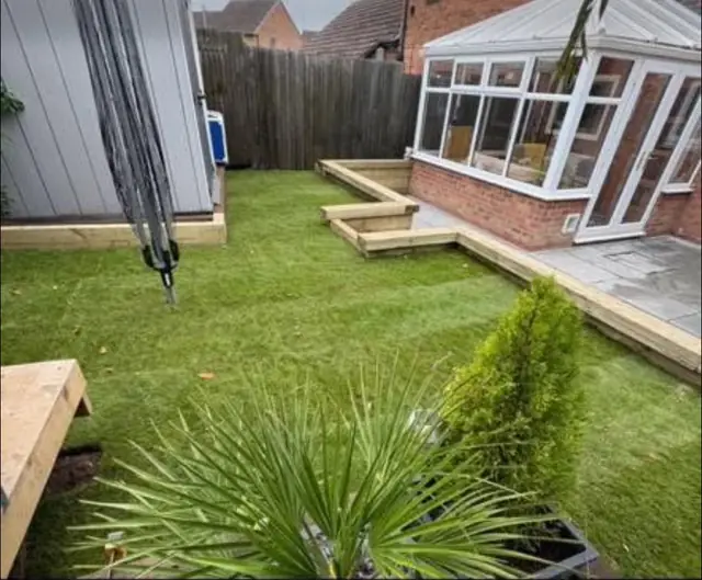 A lawn and sleeper edged patio in the corner of a garden