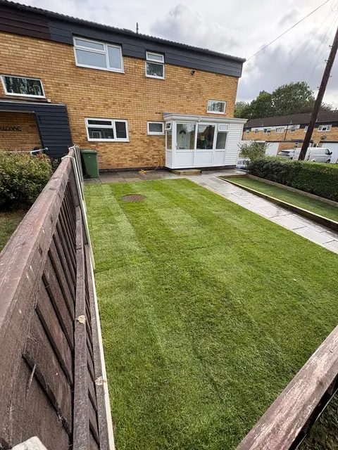 A wide new lawn with a slab border and path, seen from the fence line